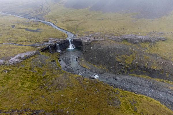 Aerial view of a river with multiple small waterfalls in a rocky, mossy landscape under a foggy sky.