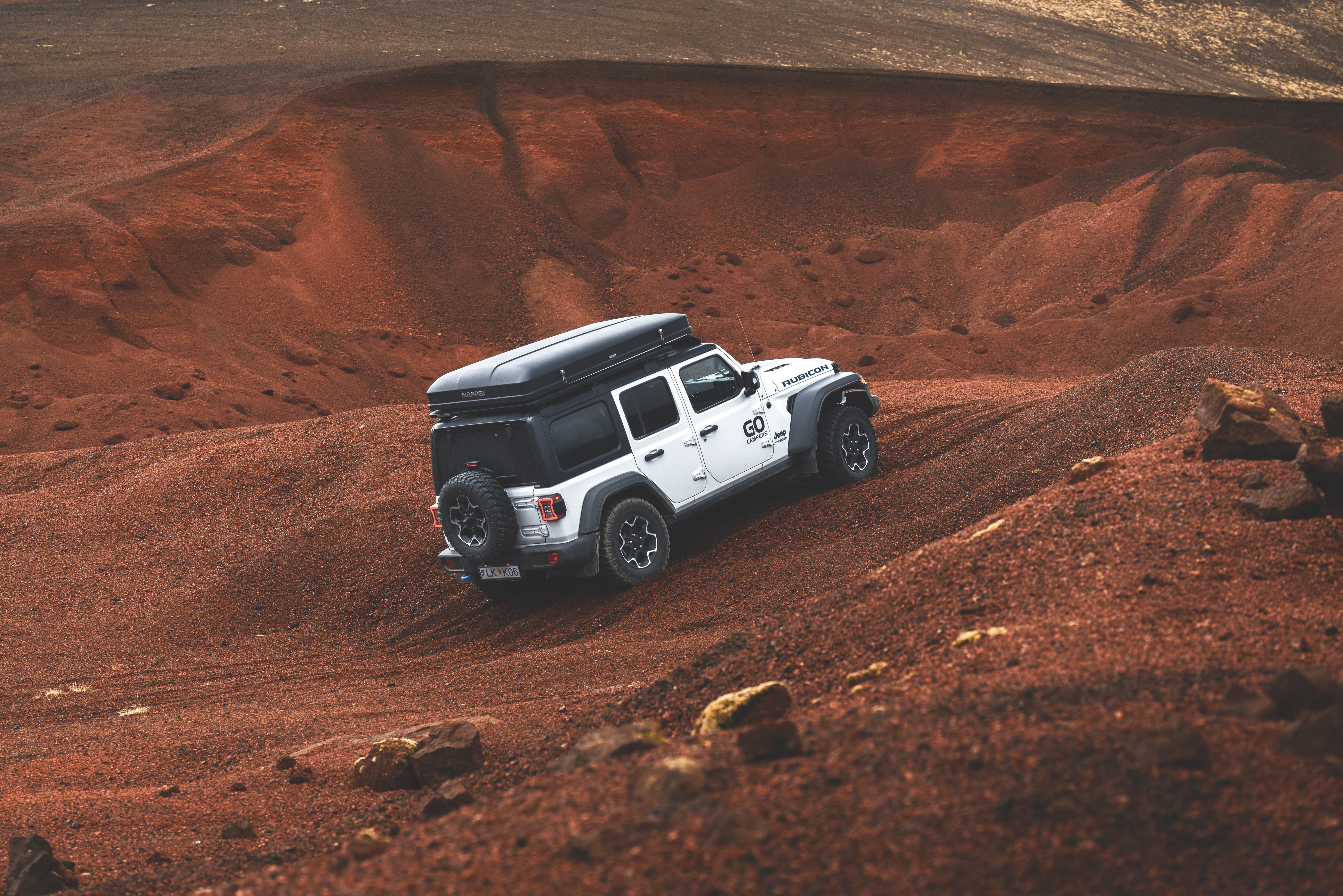 A 4x4 campervan that sleeps 4 driving through red gravel hills, camper van rental Iceland