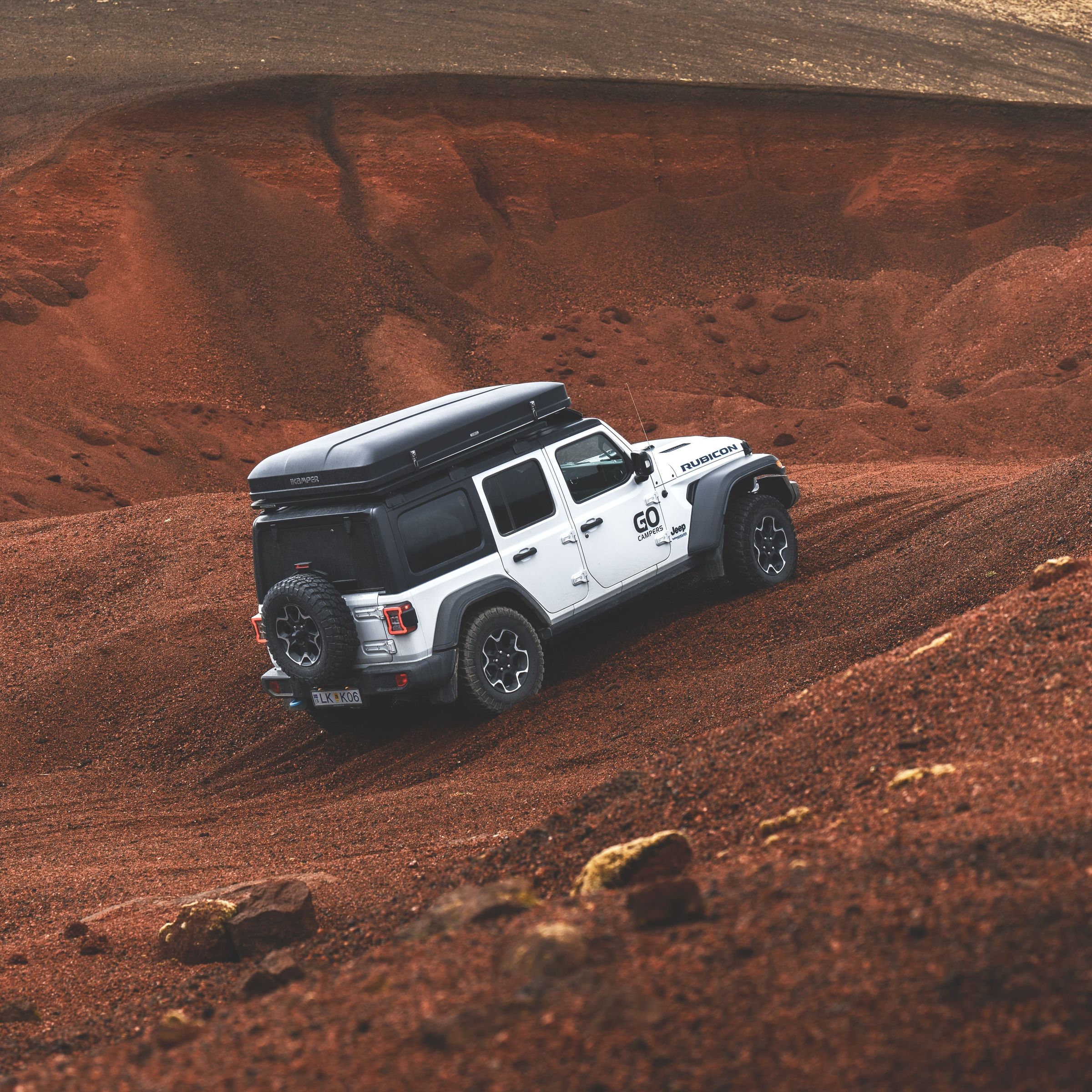 White Jeep with a roof tent climbing a red, rocky hill.