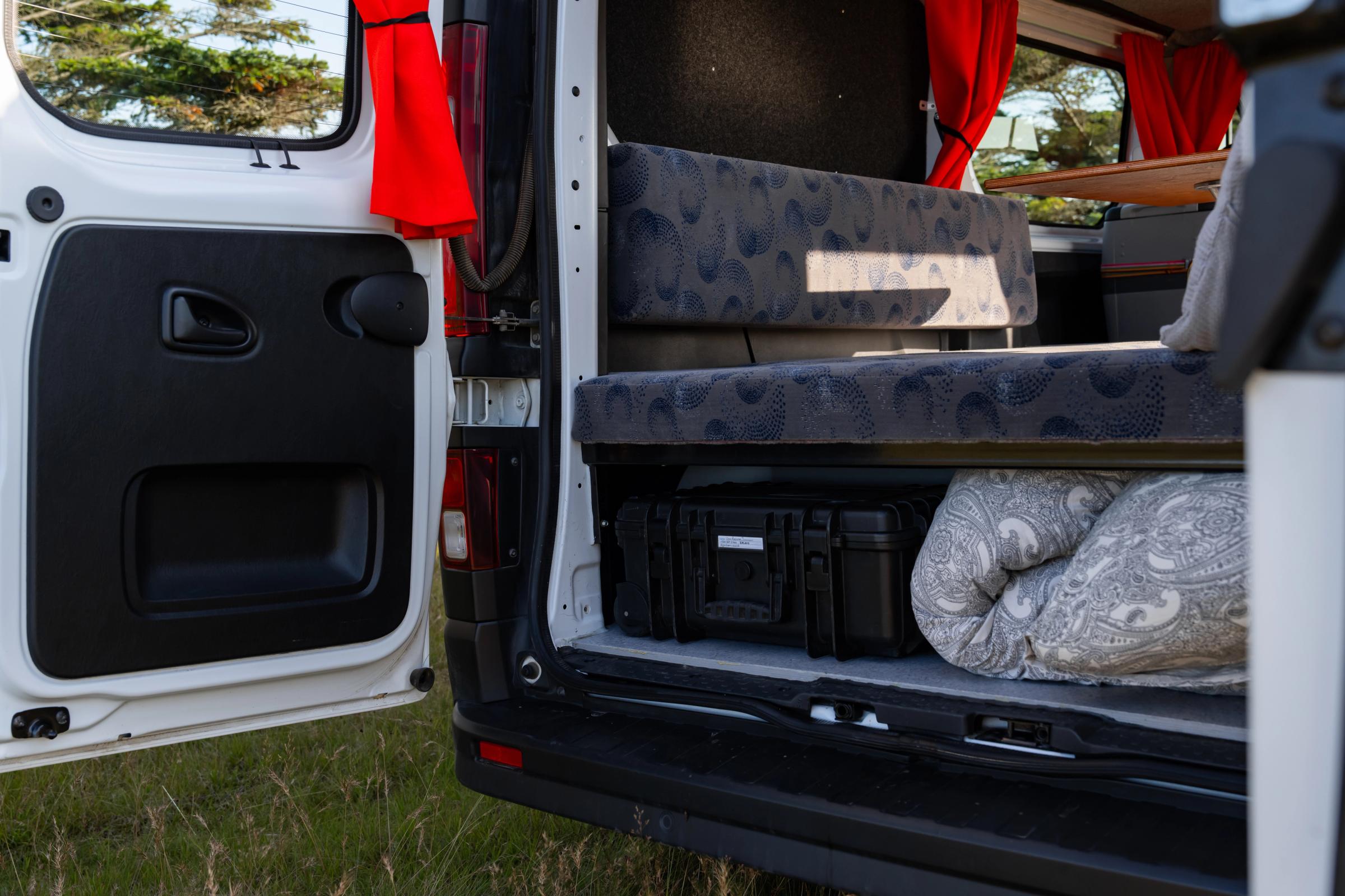 Storage space under the rear bench holding a black storage case and rolled bedding