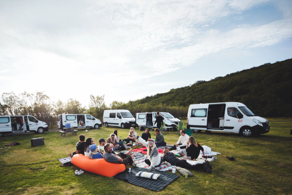 Group of people sitting on a picnic blanket surrounded by campervans