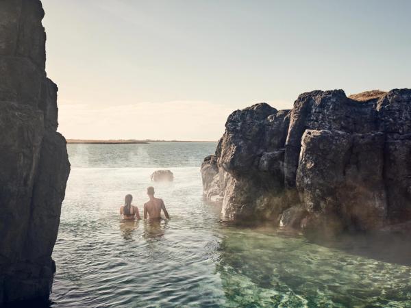 a man and a woman are swimming in a hot spring surrounded by rocks .