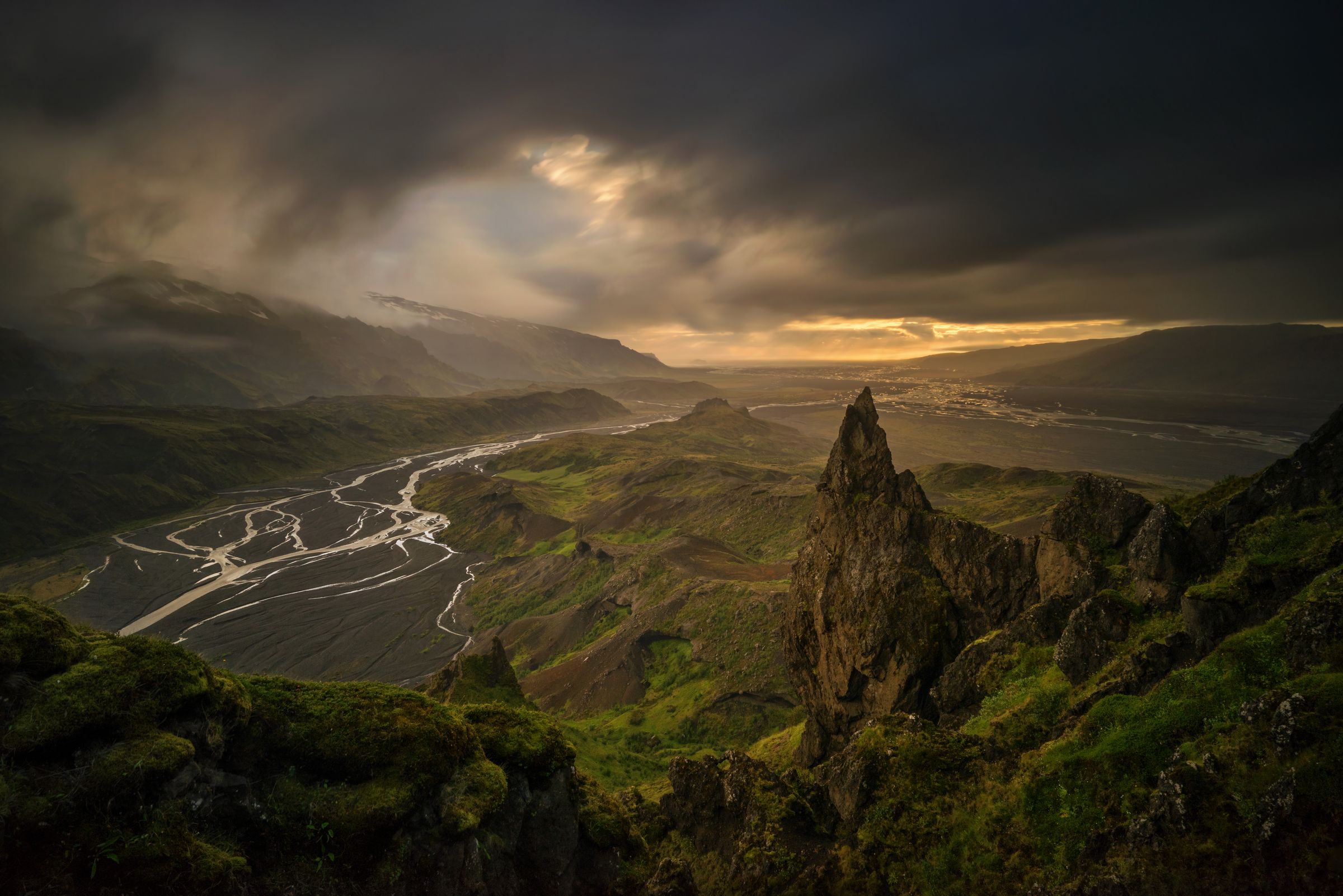 une rivière qui coule à travers une vallée entourée de montagnes sous un ciel nuageux à Þórsmörk en Islande.