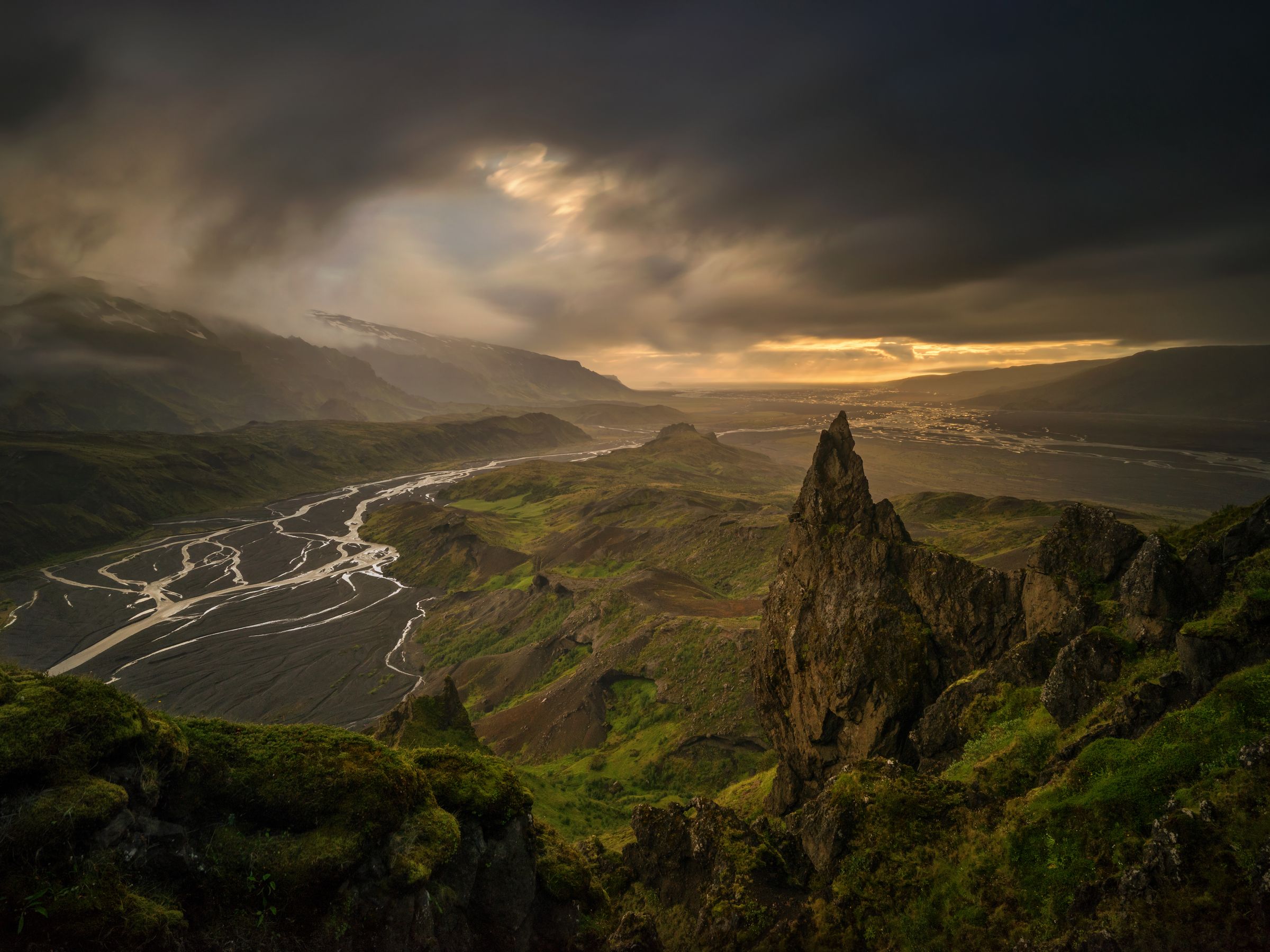 une rivière qui coule à travers une vallée entourée de montagnes sous un ciel nuageux à Þórsmörk en Islande.