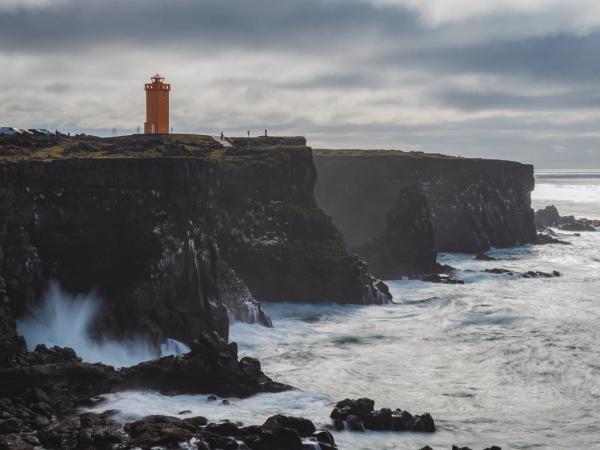 paisaje con acantilados donde rompen las olas del mar con un faro naranja encima