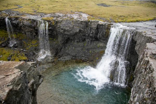 Two waterfalls cascade into a clear blue pool surrounded by rocky cliffs.