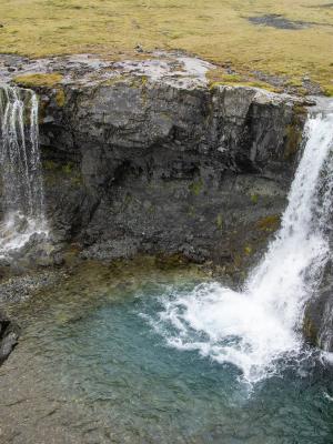 Two waterfalls cascade into a clear blue pool surrounded by rocky cliffs.