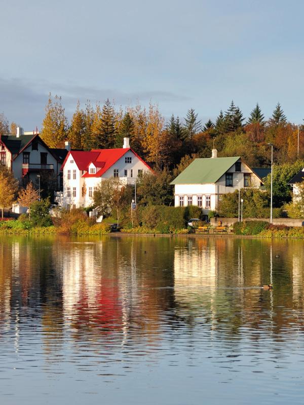 Houses with colorful roofs and autumn trees reflected in a calm lake.
