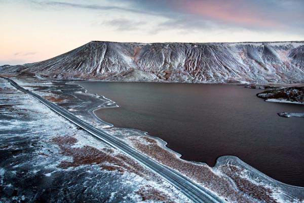 an aerial view of a road leading to a lake surrounded by snow covered mountains in iceland.