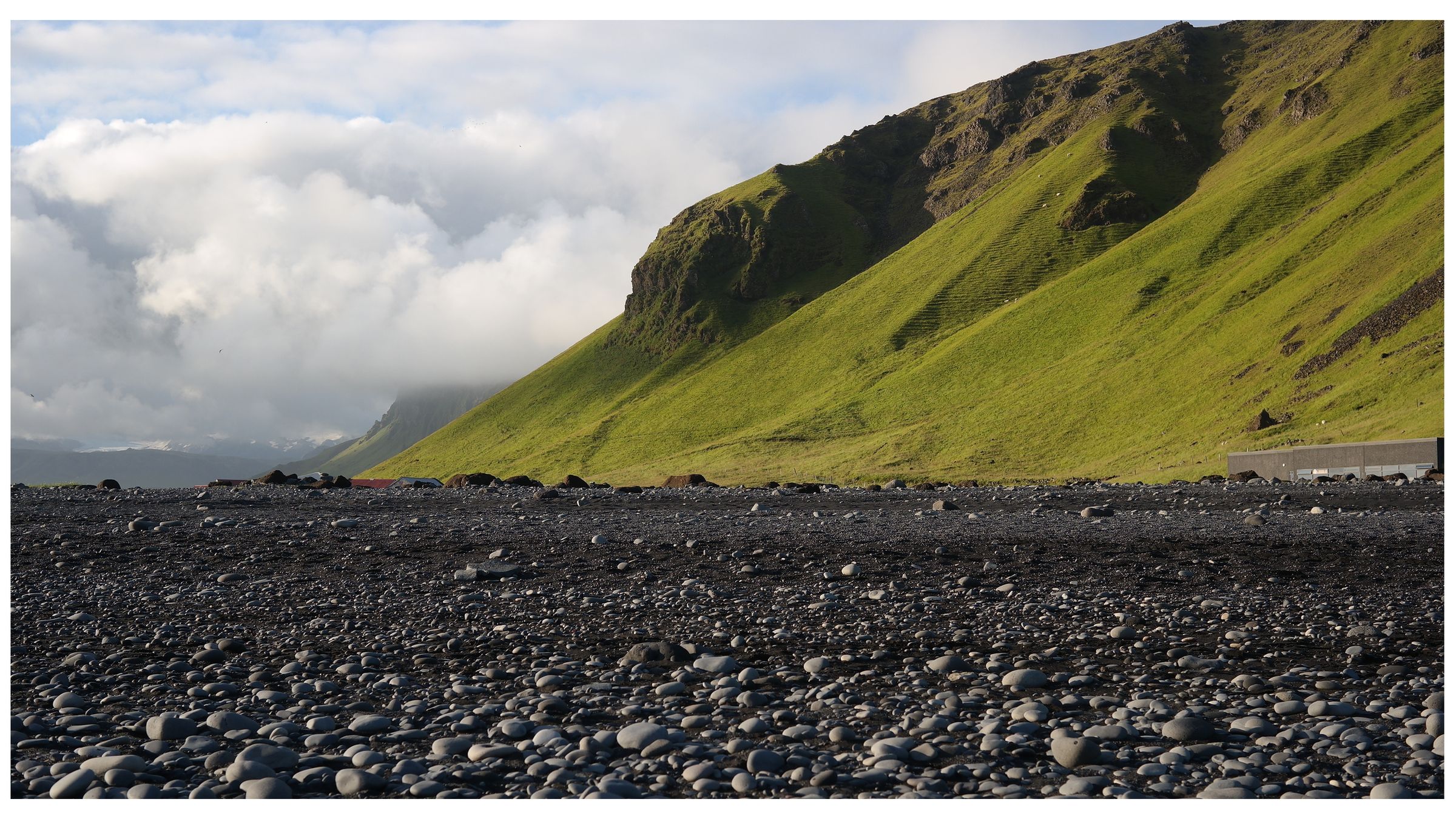 black pebbles on a black sand beach with a cliff covered by moss