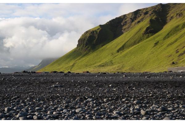 black pebbles on a black sand beach with a cliff covered by moss