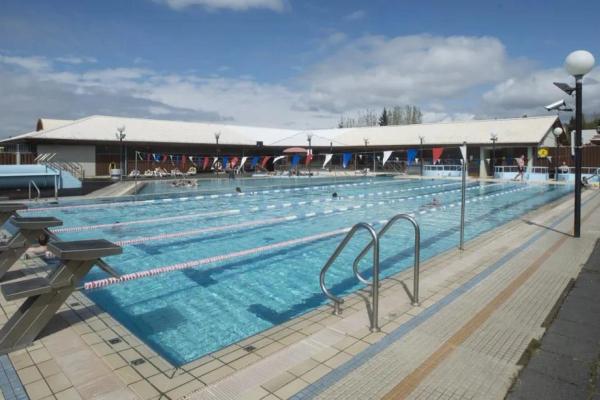 a large swimming pool with a building in the background and people swimming in it .