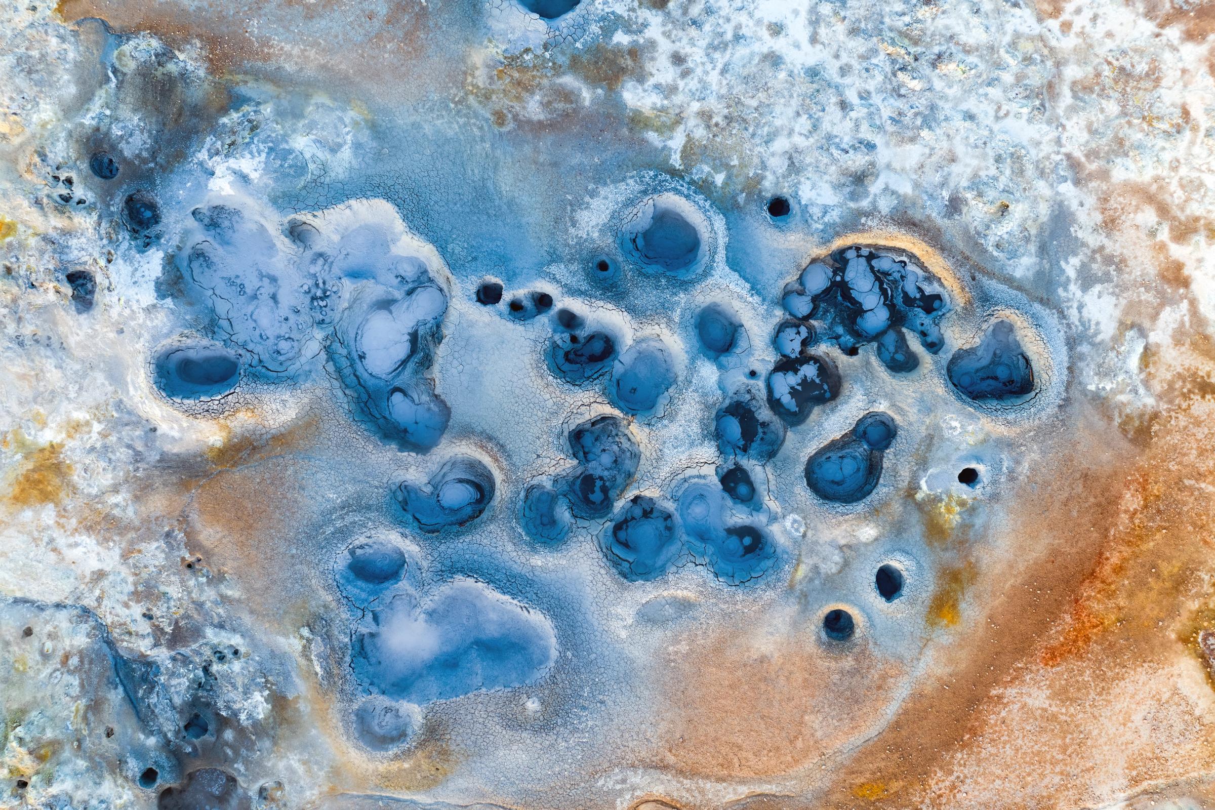 Piscinas geotérmicas azules en un paisaje de tierra blanca y marrón rojiza.