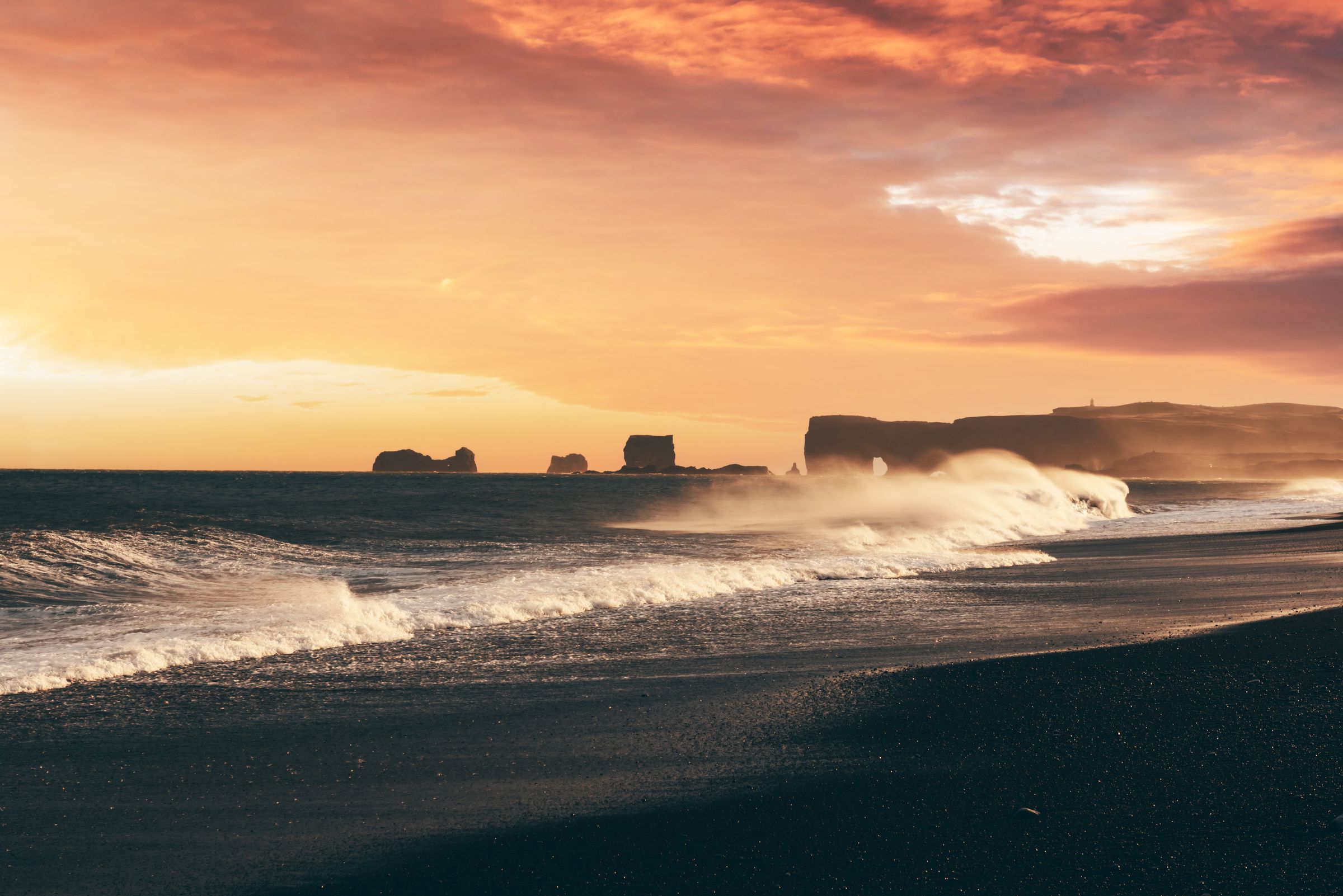 le soleil se couche sur l'océan et les vagues se brisent sur la plage de Reynisfjara en Islande.