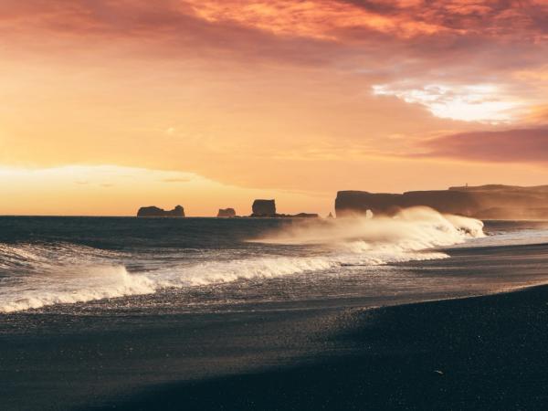 le soleil se couche sur l'océan et les vagues se brisent sur la plage de Reynisfjara en Islande.