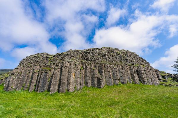 Basalt columns rising from a green field under a cloudy blue sky.