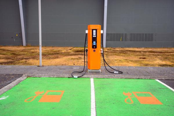 An orange electric vehicle charging station next to two green parking spots with electric car symbols.