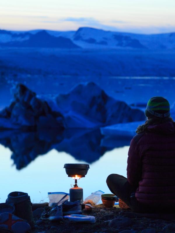 una persona está sentada en la orilla de un lago con una estufa frente a ella .