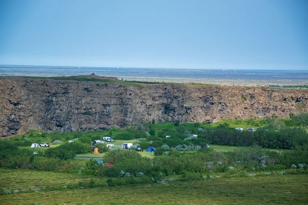 a group of tents are sitting in a field in front of a large rock wall .