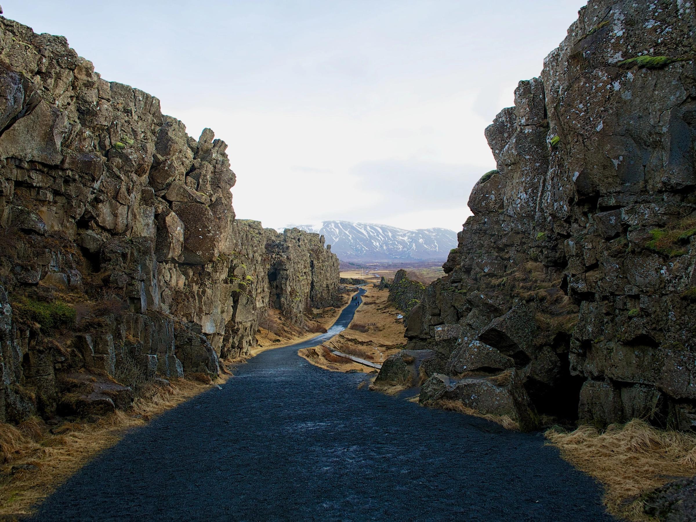a road between two rocky cliffs with mountains in the background .