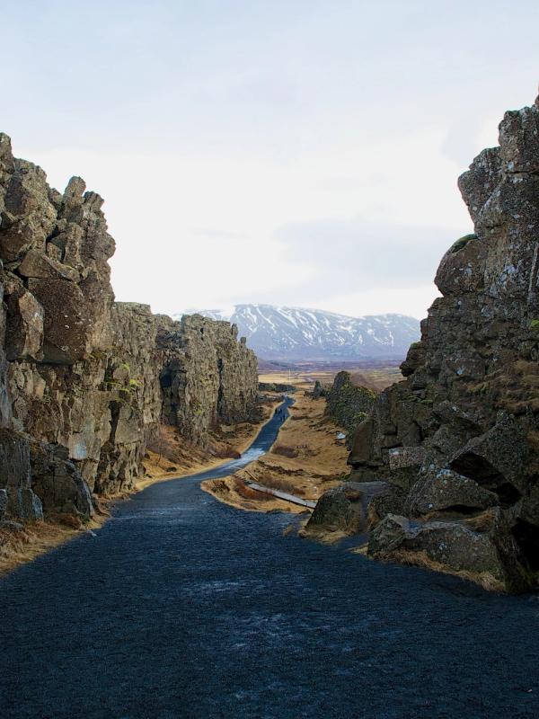 a road between two rocky cliffs with mountains in the background .