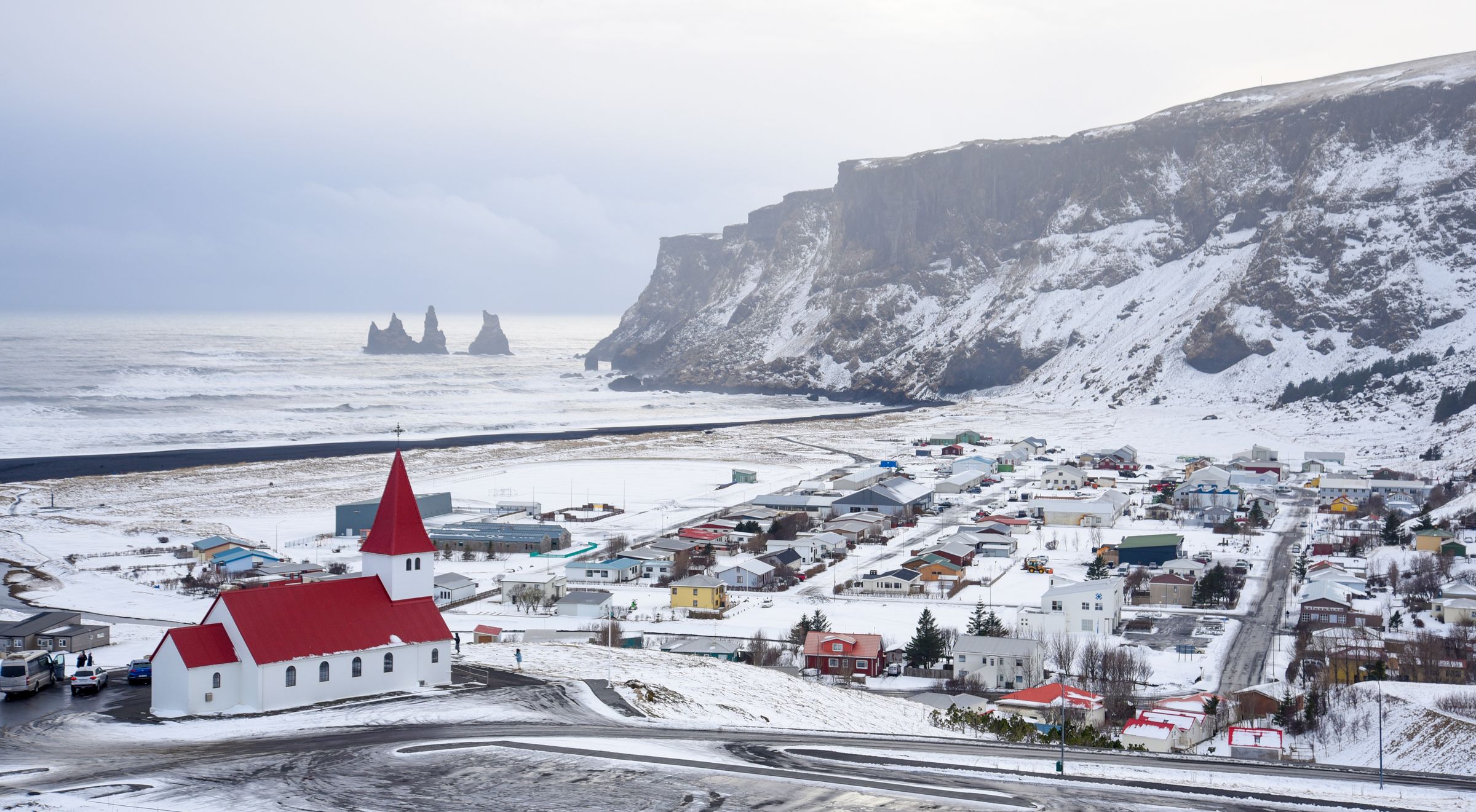 there is a church with a red roof in the middle of a snowy town in vík in iceland.
