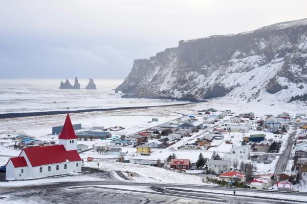 there is a church with a red roof in the middle of a snowy town in vík in iceland.