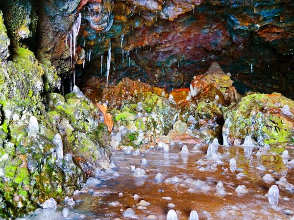 Colorful ice cave interior with icicles, mossy rocks, and icy ground.
