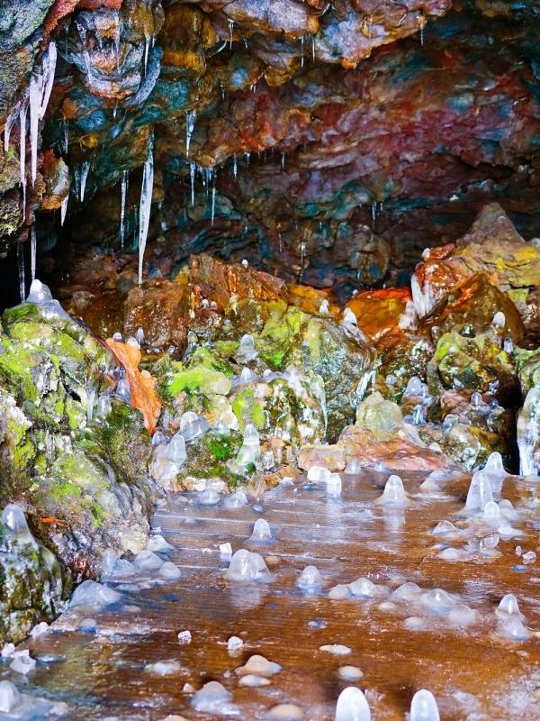 Colorful ice cave interior with icicles, mossy rocks, and icy ground.