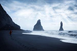 a person is walking on a black sandy beach near the ocean .