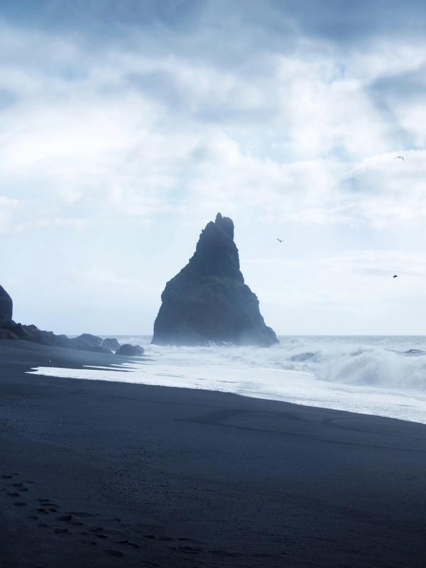 a person is walking on a black sandy beach near the ocean .