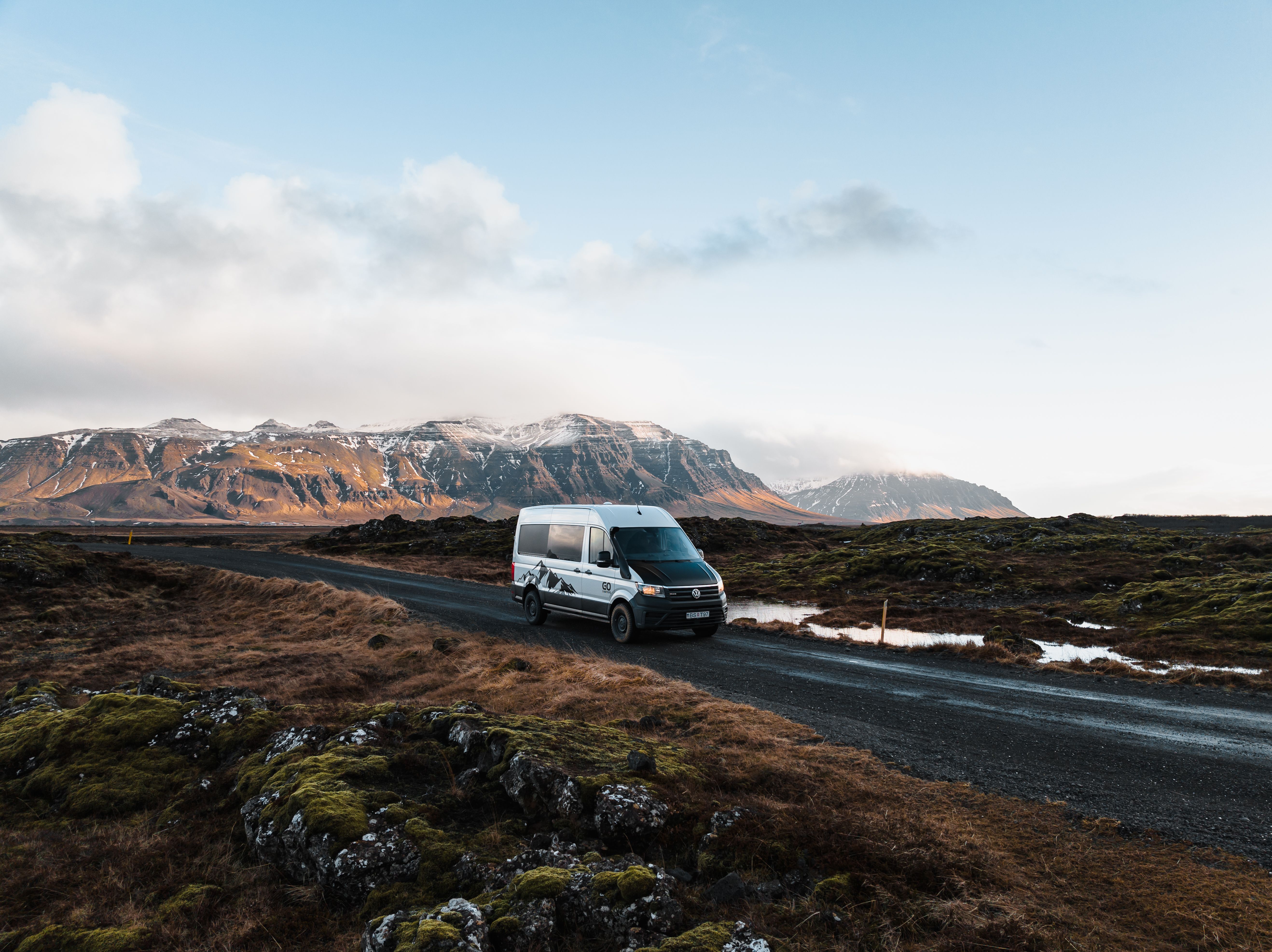 Una autocaravana 4x4 circulando por una carretera asfaltada a través de un campo de lava, alquiler de autocaravanas en Islandia
