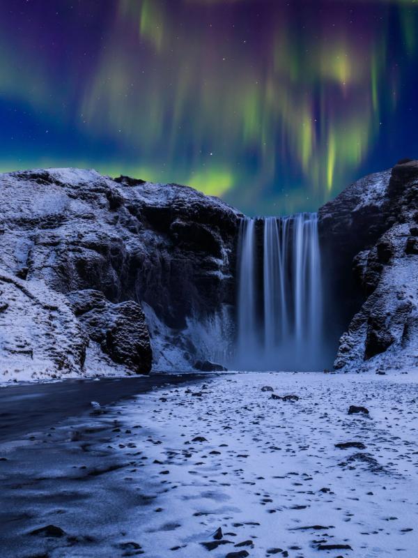 Skógafoss waterfall in a snowy landscape under the Northern Lights.