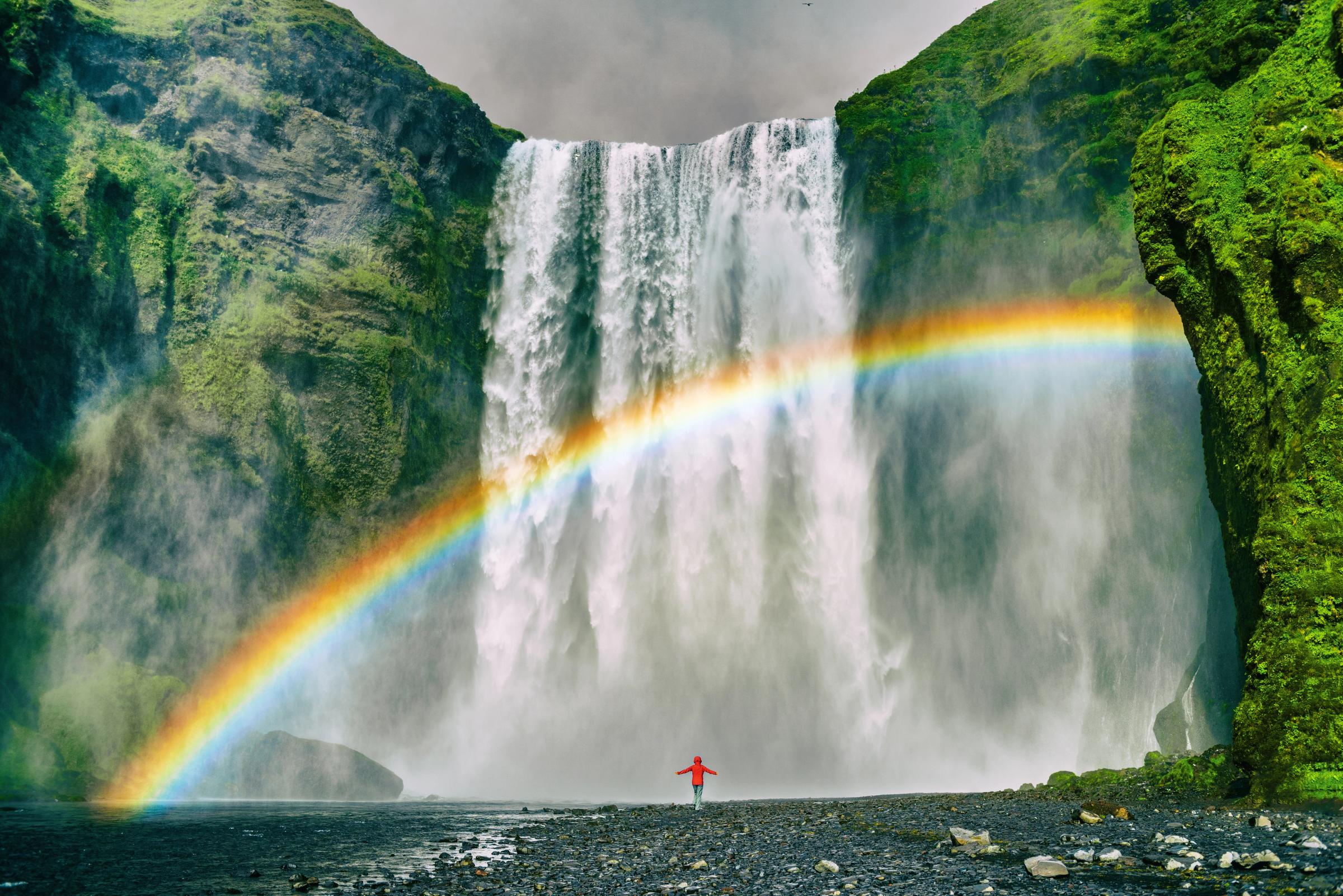 una persona está de pie frente a una cascada con un arcoíris de fondo.