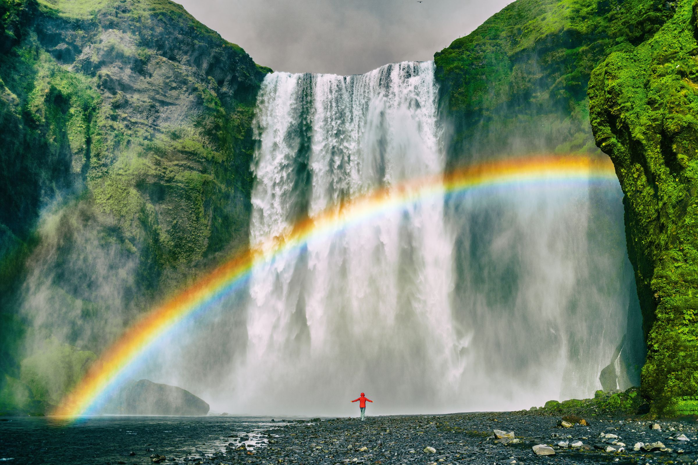 una persona enfrente de una gran cascada con el arcoíris delante