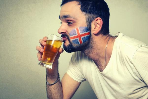 a man with an Icelandic flag painted on his face is drinking a glass of beer .
