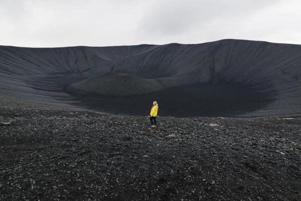 a person in a yellow jacket is standing in front of a large crater .