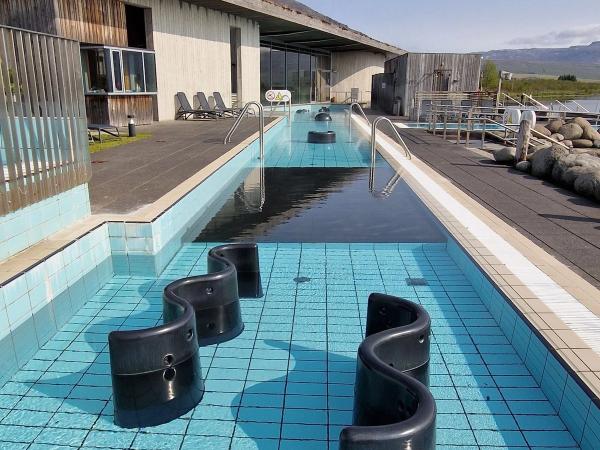 Outdoor geothermal pool with S-shaped water features, a modern building, and distant mountains.