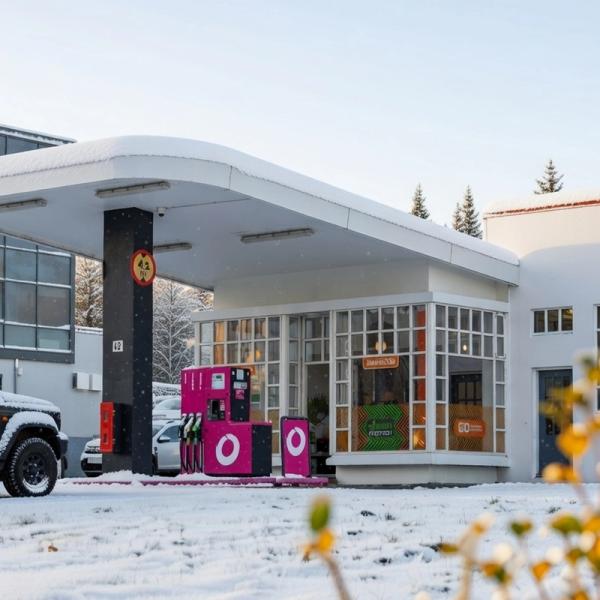 A black SUV at a gas station with bright pink pumps and a white building.