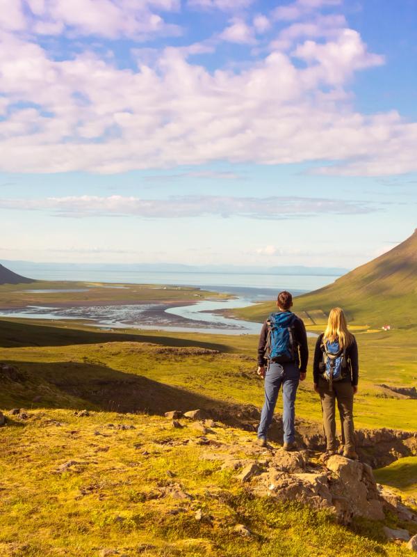 a man and a woman are standing on top of a hill looking at a mountain, Iceland
