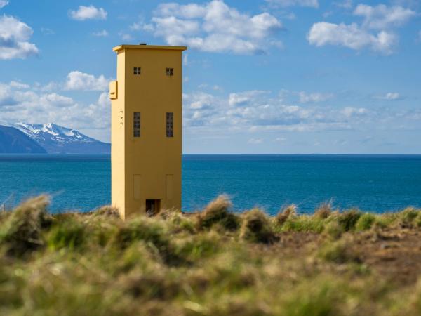a yellow lighthouse is sitting on top of a grassy hill overlooking the ocean at Húsavík in north Iceland.