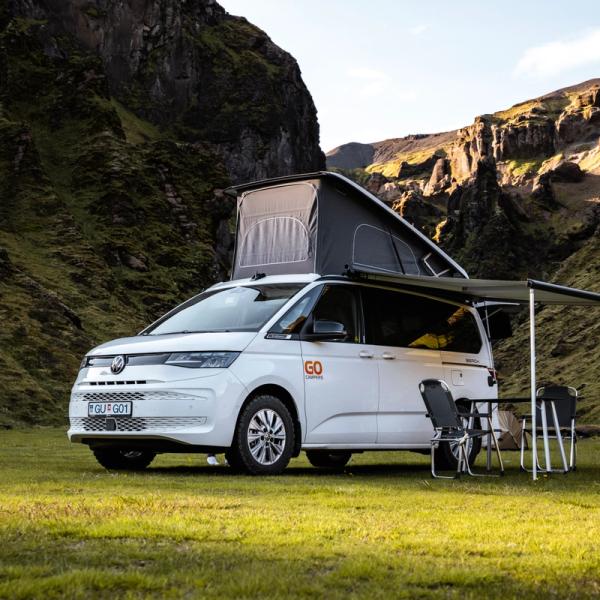 a white van with a pop top roof is parked in a grassy field .
