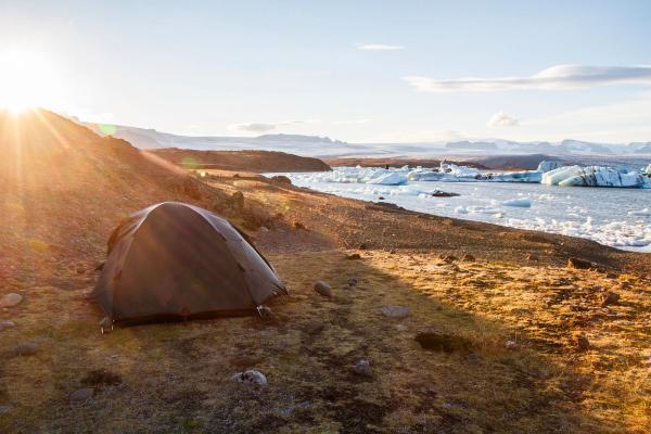 a tent is sitting on the shore of a glacier lake .