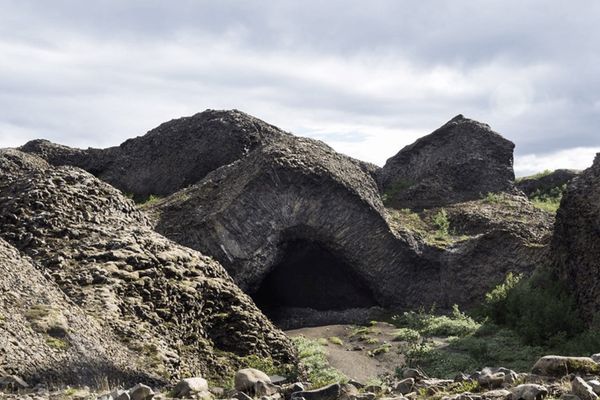 a cave in the middle of a rocky hillside with a cloudy sky in the background at hljóðaklettur in iceland.