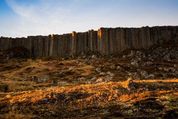 Basalt column cliffs rising above a rocky, grassy hillside, bathed in golden light.