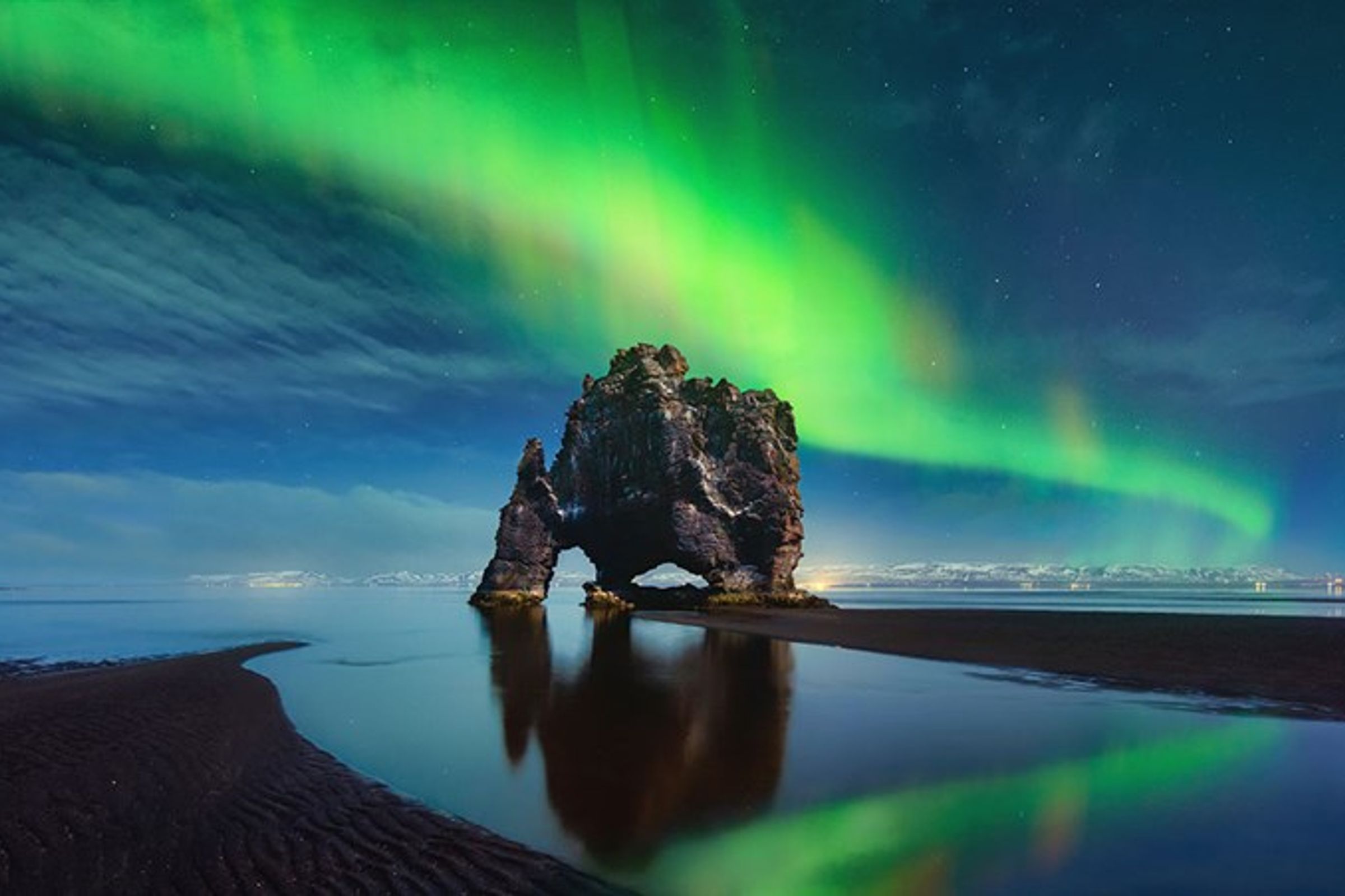 the aurora borealis is shining over a rock formation in the middle of the ocean .