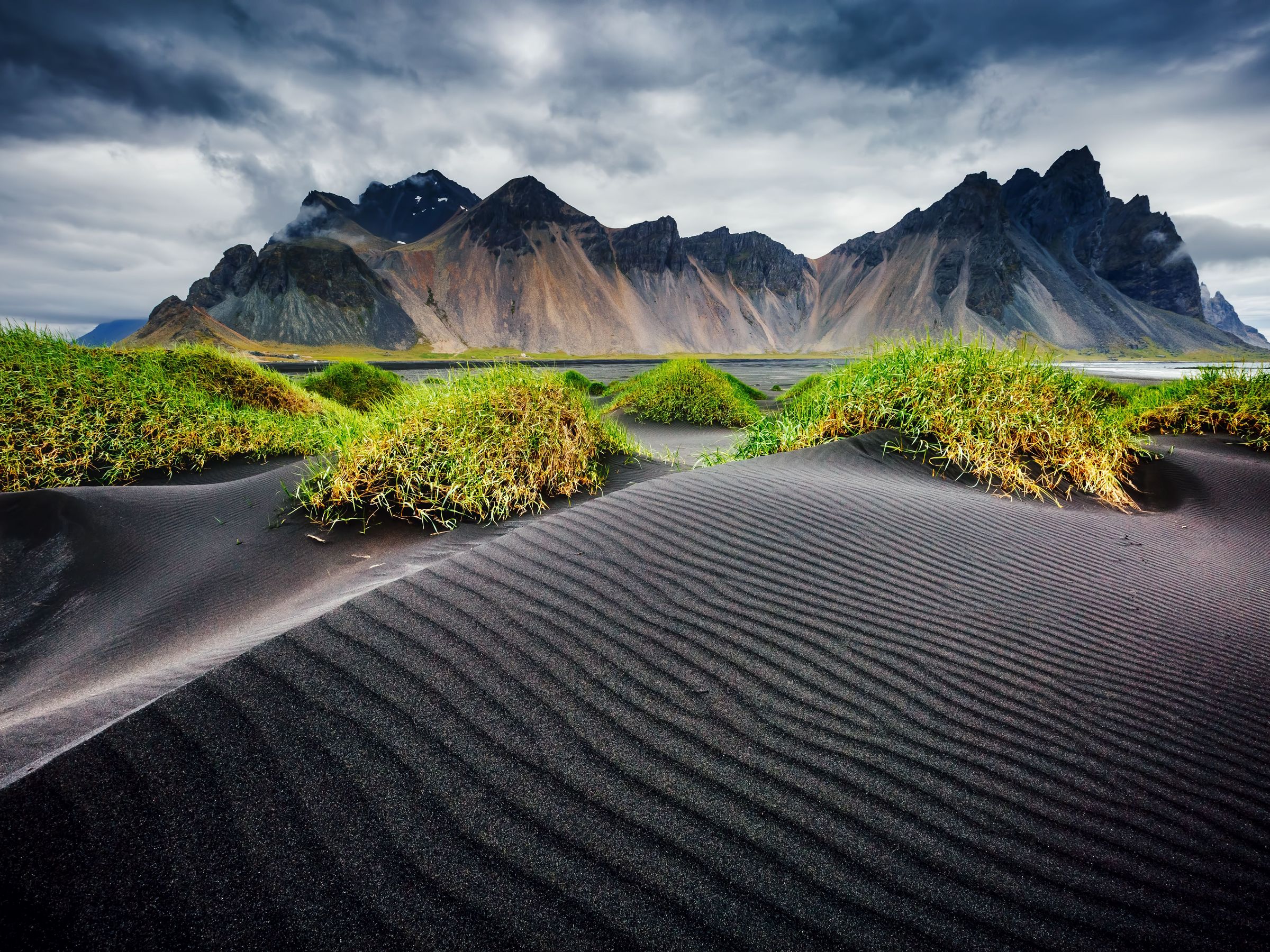 a desert landscape with mountains in the background and a black sand dune in the foreground .
