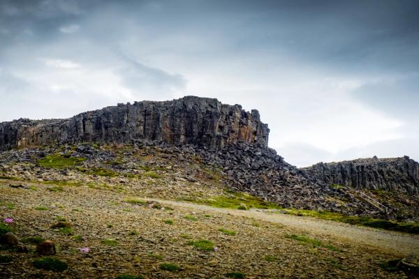 A rugged, rocky landscape with a dark cliff of columnar basalt formations under an overcast sky.