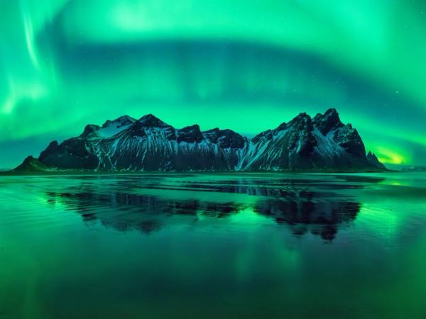 the aurora borealis is reflected in the water over the mountains .