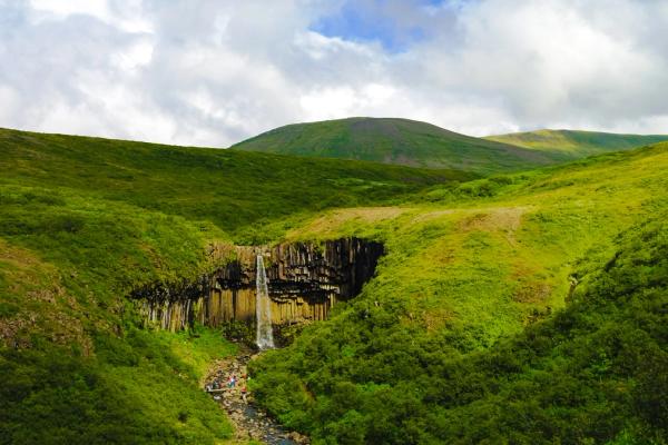 a waterfall set in a bowl of lava rock and surrounded by forest